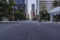 a truck and cars are sitting on a empty street in the city, with tall buildings and trees