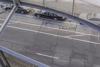 black car in parking lot with a couple cars under pedestrian bridge above road level area