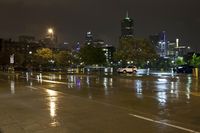 a wet street with a city in the background at night while vehicles are passing by