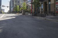 the empty sidewalk has green trees on both sides of it and buildings in the background