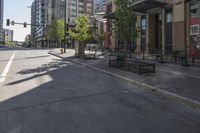 the empty sidewalk has green trees on both sides of it and buildings in the background