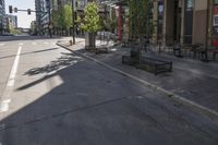 the empty sidewalk has green trees on both sides of it and buildings in the background