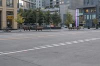 two people skateboard on a city street in front of buildings with people standing around