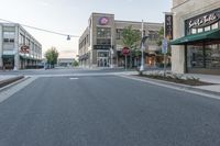 a wide empty street is shown in front of stores, and businesses in the background