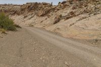 a dirt road is shown in the desert with rocks, bushes and boulders in the background