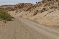 a dirt road is shown in the desert with rocks, bushes and boulders in the background