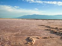 a barren desert is pictured under an blue sky with a mountain in the background,