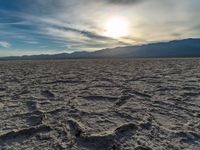 the sun rising on a salt flat desert landscape with mountains in the background at sunset