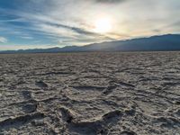 the sun rising on a salt flat desert landscape with mountains in the background at sunset