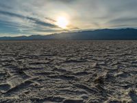 the sun rising on a salt flat desert landscape with mountains in the background at sunset