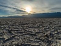 the sun rising on a salt flat desert landscape with mountains in the background at sunset