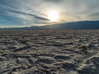 the sun rising on a salt flat desert landscape with mountains in the background at sunset