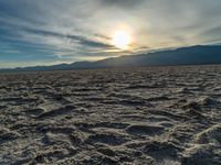 the sun rising on a salt flat desert landscape with mountains in the background at sunset