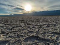 the sun rising on a salt flat desert landscape with mountains in the background at sunset