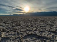 the sun rising on a salt flat desert landscape with mountains in the background at sunset