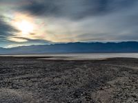 a deserted desert landscape with dark clouds over the mountain range and sun shining down onto the horizon