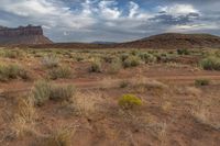 an empty dirt road winds around a large rock formation surrounded by brown grass and bushes