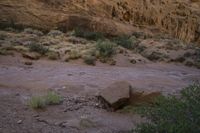 rocks in the middle of dry ground next to hills and shrubs with brown cliffs on both sides