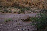 rocks in the middle of dry ground next to hills and shrubs with brown cliffs on both sides