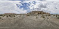 a very small patch of dirt in the desert near mountains on a cloudy day with blue skies