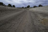 an empty dirt road passing through some dry land in the desert with a cloud over the horizon