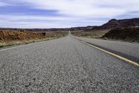 a lone stretch of highway lined with rocks and sand in the desert with blue sky and white clouds