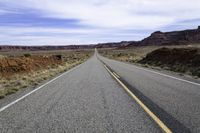 a lone stretch of highway lined with rocks and sand in the desert with blue sky and white clouds