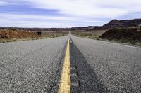 a lone stretch of highway lined with rocks and sand in the desert with blue sky and white clouds