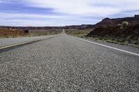 a lone stretch of highway lined with rocks and sand in the desert with blue sky and white clouds