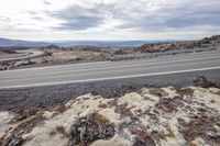 a motorcycle is traveling along a paved highway in the desert next to the mountains and an open road with hills and blue skies