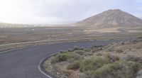 an empty highway in the middle of the desert near a mountain top and road that's not paved