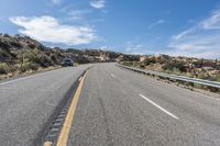 an empty road next to a mountain filled with rocks and grass under a blue sky