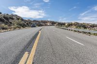 an empty road next to a mountain filled with rocks and grass under a blue sky