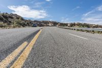 an empty road next to a mountain filled with rocks and grass under a blue sky