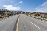 an empty road next to a mountain filled with rocks and grass under a blue sky