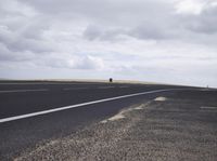 an open highway and a bench on the edge of it with a cloudy sky in the background