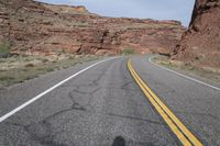 a person riding a motorcycle along a narrow road through rocks and sand cliffs a grassy area on both sides