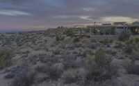 a desert house is surrounded by shrubs and plants in the evening sky during the day