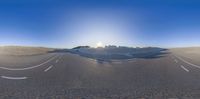 an intersection in the desert with some sand on it and sun shining behind it and two empty road signs,