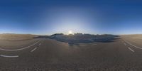 an intersection in the desert with some sand on it and sun shining behind it and two empty road signs,