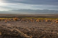 a lone red fire hydrant is standing in the desert near the mountains with sparse grass