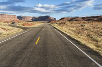 an empty desert road stretches from the vast open sky with a lone tree standing in the foreground