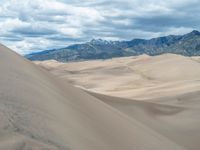 a person riding a horse through a wide expanse of sand dunes and mountains behind them