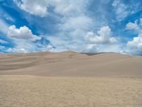 a brown sand dune surrounded by clouds on a blue sky day by julia goyer for stockstuck