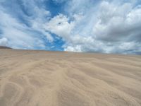 a lone desert with large sand dune in the middle and clouds overhead over it and blue sky