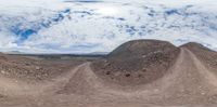 several mounds and a dirt road on a sunny day in the desert, with an airplane above it