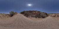 a large rock with dirt trail near it in desert area under full moon sky in daytime