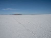 a car driving across a large open plain covered in snow on a sunny day by itself