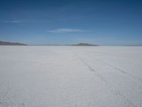 a car driving across a large open plain covered in snow on a sunny day by itself