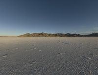 the bare desert has many footprints of people on it, with mountains in the background